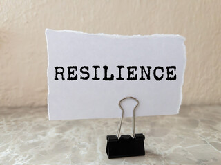 Resilience message written on ripped torn white paper piece on wall background. Conceptual...
