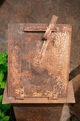 Heavily rusted metal box with a diagonal bar and hinges, showing signs of significant age and wear.