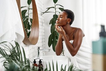 Young woman performs skincare routine in bright bathroom surrounded by plants in morning light