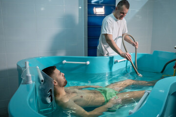 Therapeutic Water Bath.Man relaxing in hydrotherapy bath while therapist adjusts water settings.