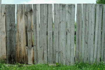 Fototapeta premium A weathered wooden fence of varying shades of grey and brown stands on green grass against a pale sky.