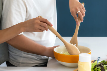 Close up of two people holding spoon and fork mixing salad in bowl