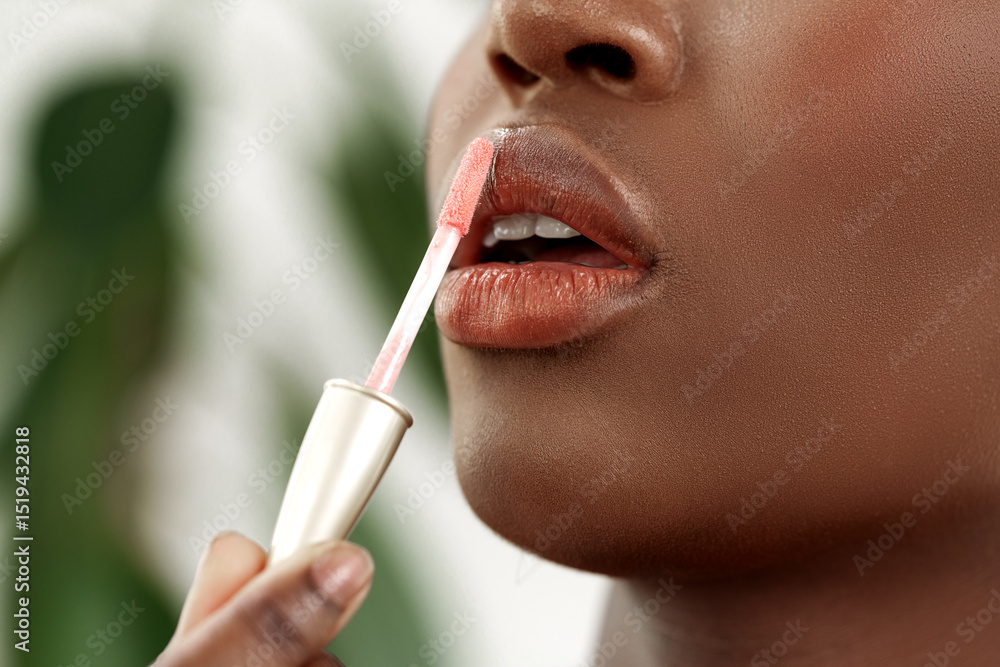 Poster woman applying lip gloss in a natural setting with greenery in the background during daylight hours