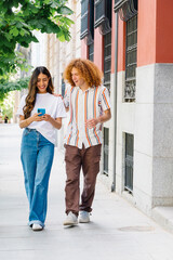 Young couple walking along urban street, browsing smartphone together, exchanging cheerful glances during warm sunny afternoon