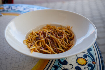 Spaghetti bolognese with meat sauce served in white bowl on ceramic mosaic table outdoors. 