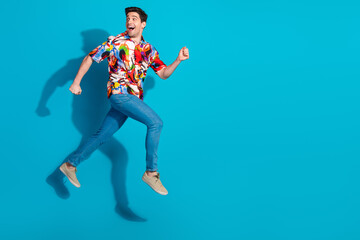 Dynamic young man in trendy outfit jumping energetically against a vibrant blue background