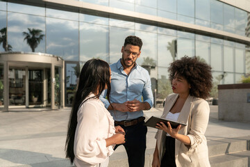 Three multiracial Business people discussing work using tablet standing outside office building