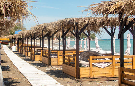 A beach with a row of wooden cabanas and umbrellas