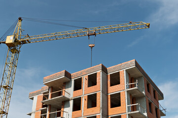 Tower crane rises above unfinished brick apartment building, symbolizing progress and growth in urban construction under a bright blue sky.