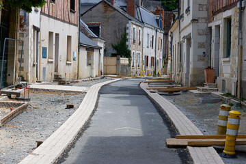 Fototapeta premium Narrow street under construction in a European town, with old buildings lining the sides and construction materials scattered around.