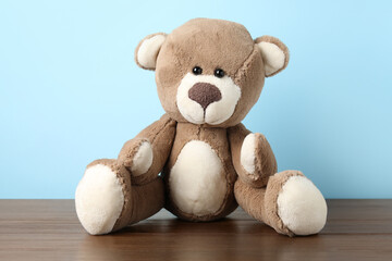 Cute teddy bear on wooden table against light blue background