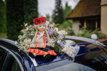 Close-up of a wedding car decorated with a doll in traditional attire and a bouquet of lilac and...