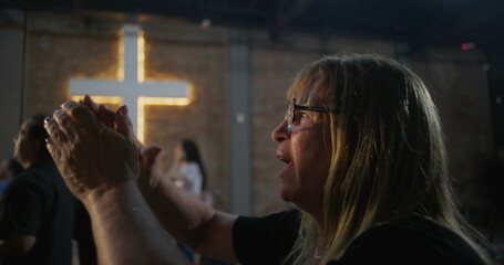 Arms raised in worship during a church service, glowing cross in background, powerful expression of spiritual devotion, faith, and praise in a sacred community setting