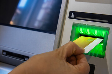 ATM Card Entering Illuminated Slot. Cash machine card reader slot glowing green as a card is inserted by person hand.