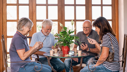 A cheerful group of older adults socializing with smartphones sit together around a glass coffee...
