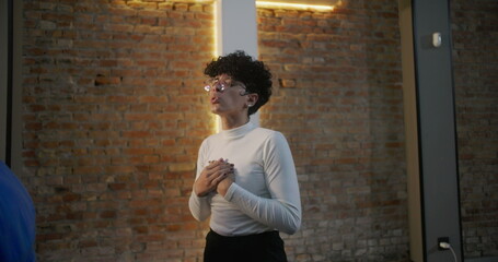 Young woman standing in church with hands clasped on chest, engaged in prayer and reflection, brick...