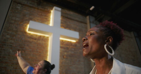 African American woman singing passionately during worship service, illuminated cross in...