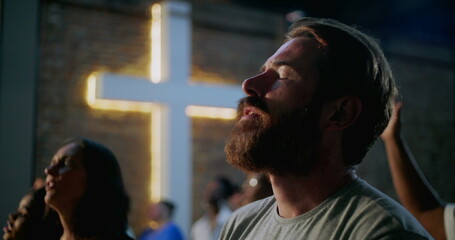 Man praying with eyes closed during worship in church setting, emotional moment of faith and...
