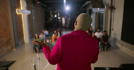Speaker addressing congregation during worship service, audience attentively seated in rows, illuminated cross on a brick wall creating a serene and inspirational atmosphere