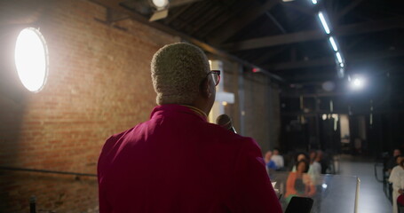Speaker delivering sermon while holding a microphone, gesturing passionately, illuminated cross on...