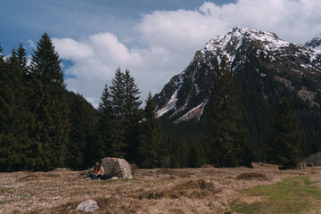 Hiker resting in a valley surrounded by fir trees and snowy mountains