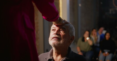 Elderly man kneeling during church blessing, hand placed on his forehead by spiritual leader,...