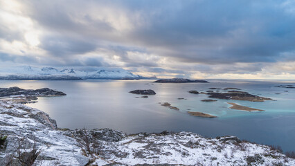 impressive, changing weather moods on the fjord between steep, snow-covered mountains around the island Kvaloya in Troms, Norway. Panorama with sea, dark clouds on the sky and snowy mountains