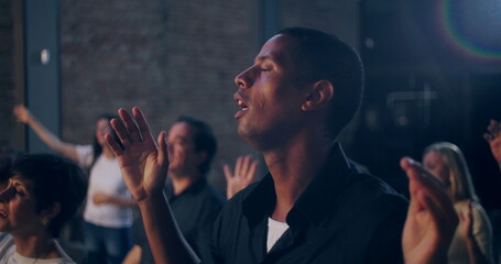 Man raising hands with eyes closed in heartfelt prayer during a spiritual gathering in a church,...