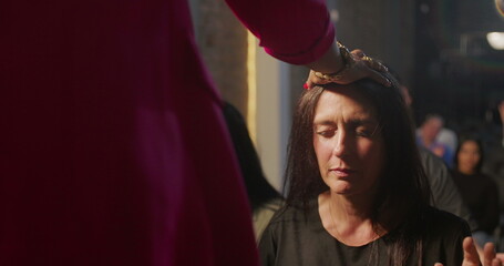 Woman kneeling during church blessing, spiritual leader touching her forehead, expression of deep...
