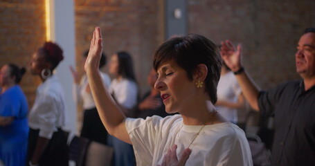 Woman raising hand in worship with heartfelt emotion during a spiritual gathering in a church,...