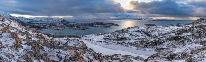 impressive, changing weather moods on the fjord between steep, snow-covered mountains around the island Kvaloya in Troms, Norway. Panorama with sea, dark clouds on the sky and snowy mountains
