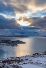 impressive, changing weather moods on the fjord between steep, snow-covered mountains around the island Kvaloya in Troms, Norway. Panorama with sea, dark clouds on the sky and snowy mountains