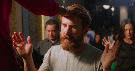 Bearded man kneeling during church blessing, spiritual leader touching his forehead, expression of...