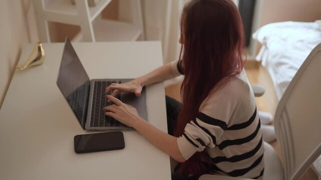 A dedicated young woman is deeply focused on her important work, skillfully typing away on her laptop in a cozy and inviting home office that beautifully blends modern design with utmost comfort