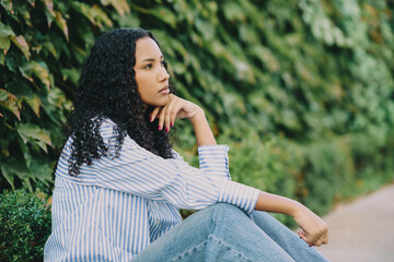 A Thoughtful Woman Lost in Nature, Sporting Beautiful Curly Hair, Dressed in Casual Attire