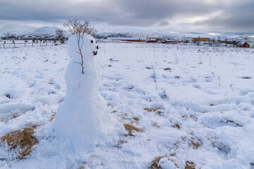snow man on hill in front of beautiful red holiday house on snowy mountain with forest and snow on meadow