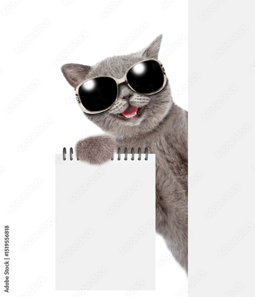 Poster Happy cat wearing sunglasses looking from behind blank white board and showing blank notepad. isolated on white background. Empty space for text