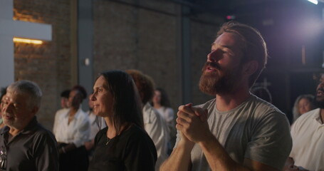 Diverse group in deep prayer, man with clasped hands in foreground showing intense devotion, surrounded by people worshiping in a spiritual gathering