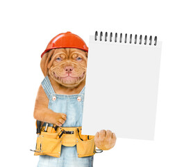 Smiling Mastiff puppy wearing hatdhat and denim overalls with tool belt shows empty list. Isolated on white background
