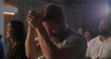 Diverse group in deep prayer, man with clasped hands in foreground showing intense devotion,...