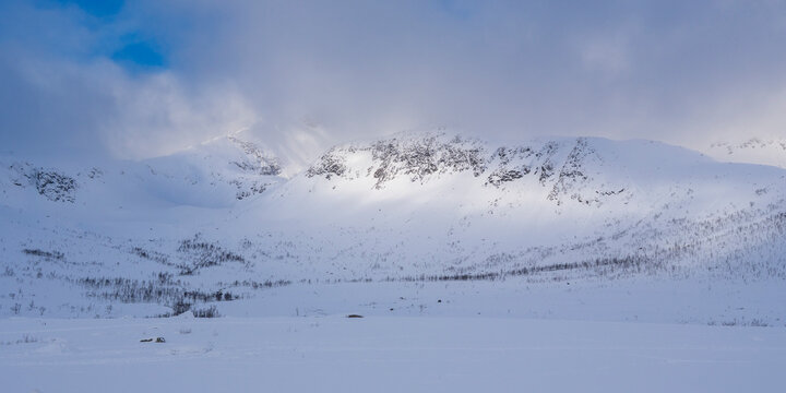 illuminated rocky mountains in the glacier-made valley, snow-covered landscape in solitude, panorama in winter wonderland Norway, with haze and fog on cloudy day, wide white snow