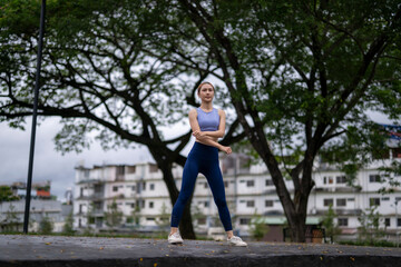 A woman is standing in a park, wearing a blue tank top and blue pants