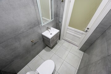 modern bathroom with gray tile, a white sink vanity, toilet, and a white door with frosted glass. A...