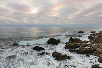 Beautiful golden hour sunset in Viña del Mar, Chile, with vibrant sky and ocean waves crashing against rugged rocks along the coastline.