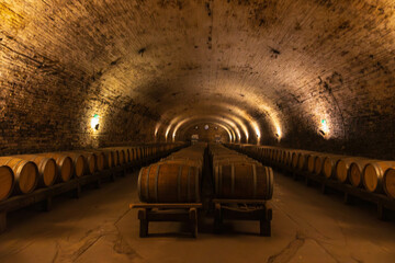 Cozy wine cellar filled with rows of wooden barrels, creating a warm yet cool atmosphere perfect...