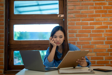 A woman is sitting at a desk with two laptops and a clipboard