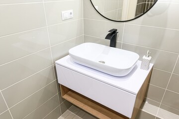Fototapeta premium modern bathroom features a white rectangular sink, black faucet, and gray tiles. A round mirror hangs above