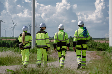 Maintenance engineer team standing at windmills at wind turbine farm. Group of people wear safety...