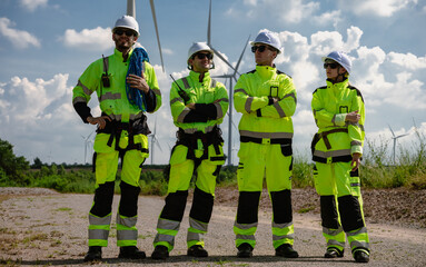 Maintenance engineer team standing at windmills at wind turbine farm. Group of people wear safety...