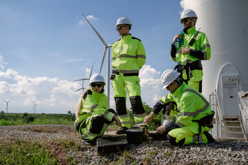 Maintenance engineer team standing at windmills at wind turbine farm. Group of people wear safety...